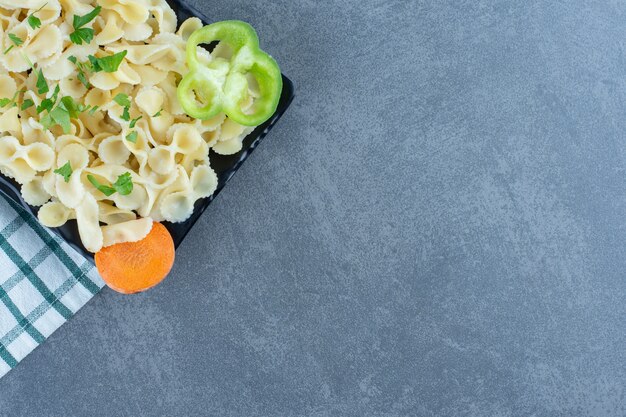Boiled pasta with vegetables on black plate. 