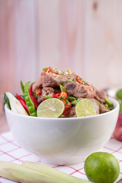 Boiled pork ribs in a white cup on a piece of fabric on a wooden table.