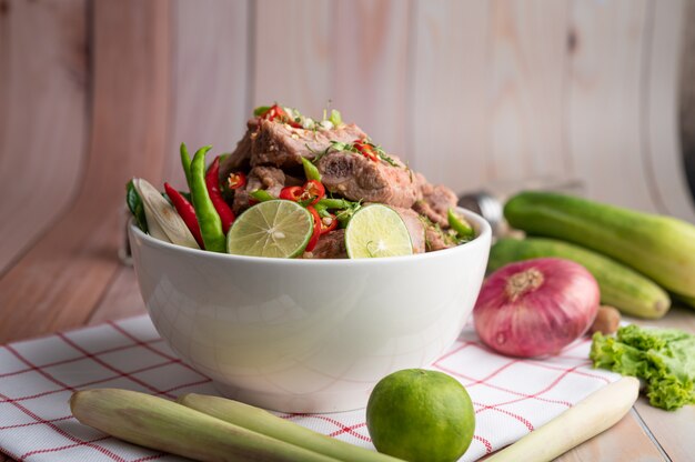 Boiled pork ribs in a white cup on a piece of fabric on a wooden table.