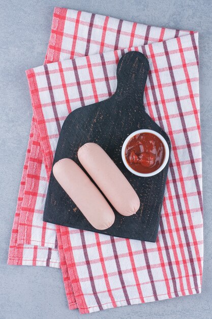 Foto gratuita salsiccia bollita e ketchup sul tagliere di legno nero.