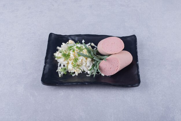 Boiled sausages and cheese on black plate.