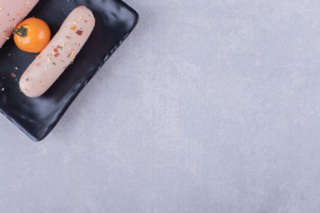 Boiled sausages and cherry tomato on black plate. 