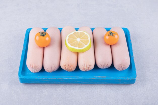 Boiled sausages decorated with lemon and tomatoes on blue plate. 