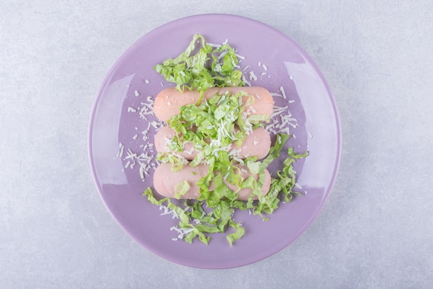 Boiled sausages decorated with lettuce on purple plate. 