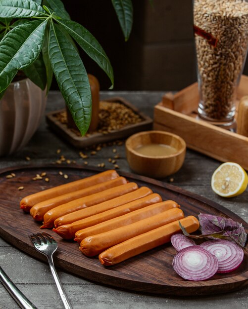 boiled sausages garnished with red onion and lemon on wooden platter