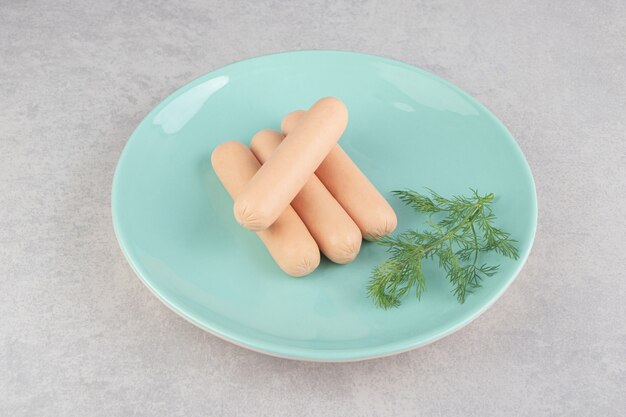 Boiled sausages and parsley on blue plate.