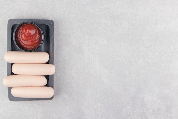 Free photo boiled sausages with ketchup on wooden board.