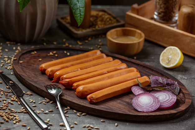 boiled sausages on wooden platter with red onion slices