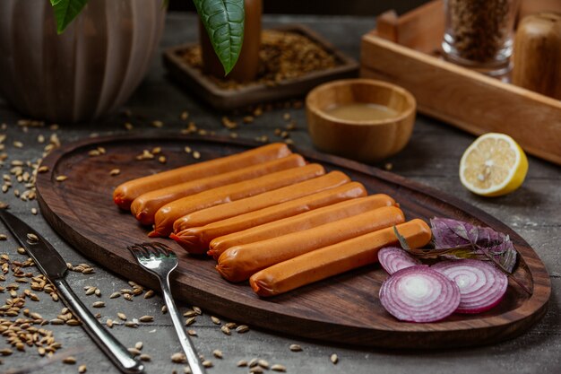 boiled sausages on wooden platter with red onion slices