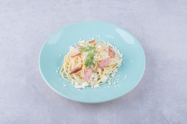 Вареные спагетти с нарезанными сосисками на синей тарелке.