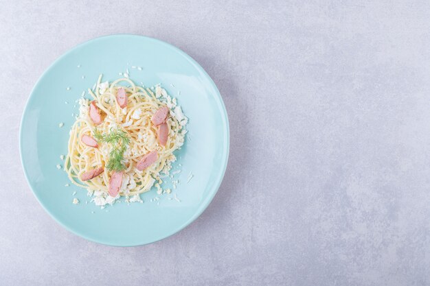 Boiled spaghetti with sliced sausages on blue plate. 