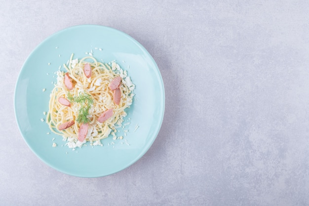 Boiled spaghetti with sliced sausages on blue plate. 