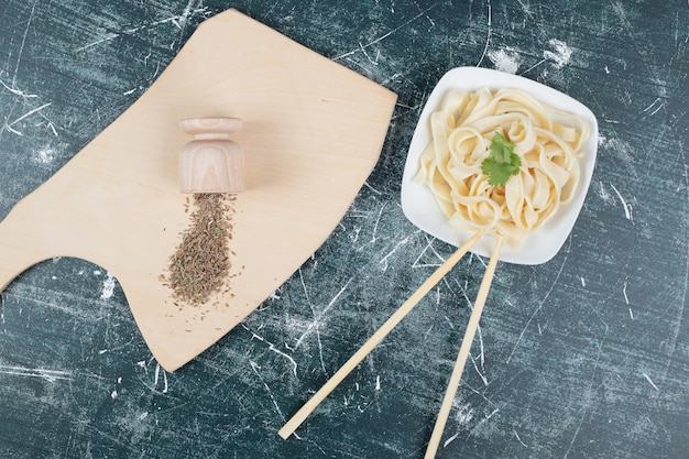 Бесплатное фото Вареные макароны тальятелле на белой тарелке с палочками для еды и специями. фото высокого качества