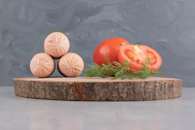 Boiled tasty sausages and tomatoes on wood piece.