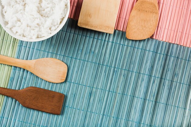 Boiled white rice bowl on different type of wooden spatula over placemat