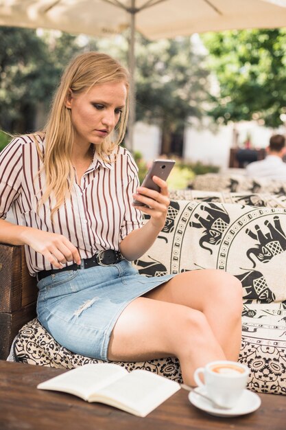 Book and coffee in front of young woman looking at mobile