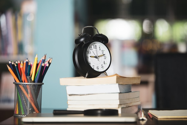 Book, laptop, pencil, clock on wooden table in library, education learning concept