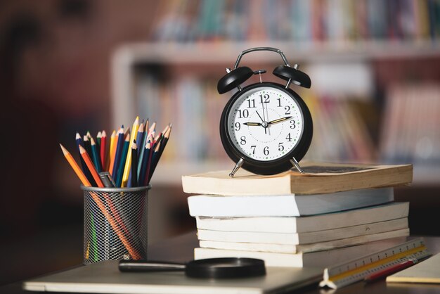 Book, laptop, pencil, clock on wooden table in library, education learning concept