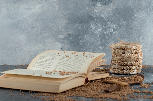 Book, raw buckwheat and crispbread on marble surface