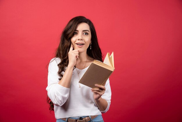 Book reading woman thinking on a red background. High quality photo