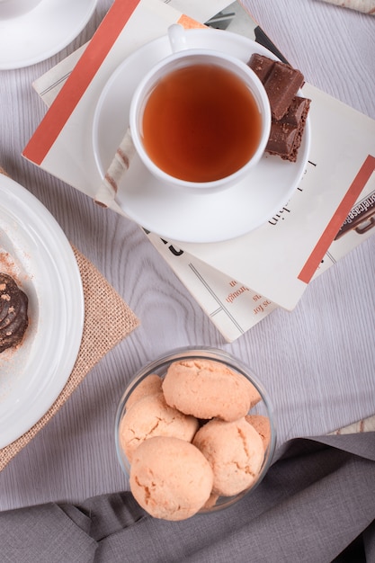 Книга, сладкие закуски и чашка чая на столе
