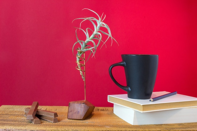 Book with cup of tea, chocolate coffer and plant on wooden background