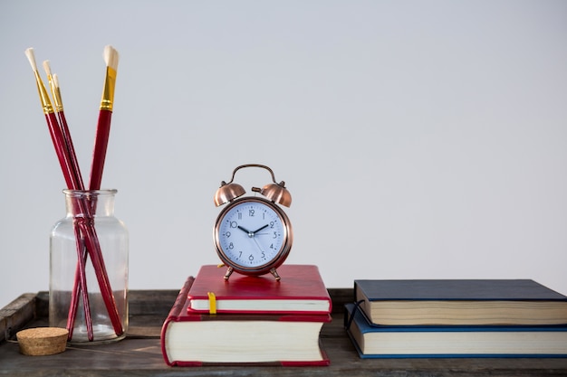 Books, alarm clock and paint brush arranged on wooden table