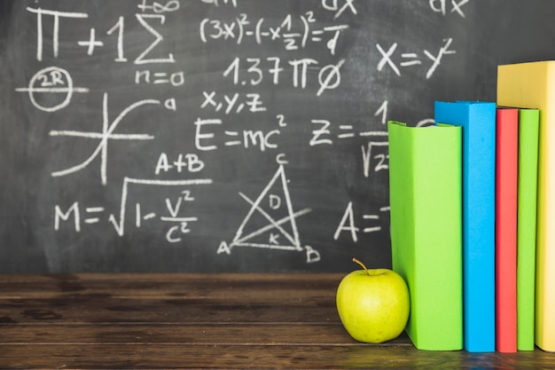 Books and apple on table near blackboard