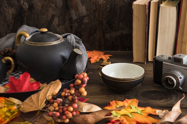 Books and camera near tea set and leaves