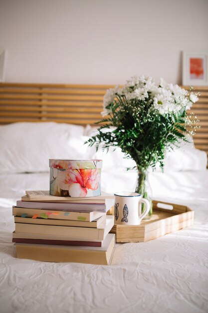 Books near tray with bouquet on bed