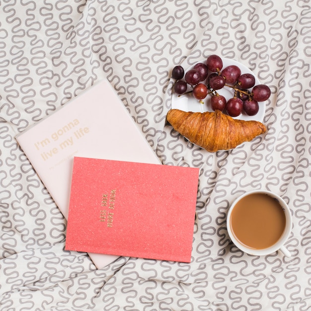 Books; tea cup; croissant and red grapes on plate over the tablecloth