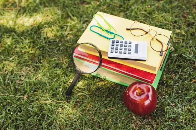 Books with optical implements, calculator and apple on grass