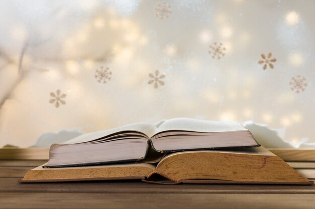 Books on wood table near bank of snow, snowflakes and fairy lights