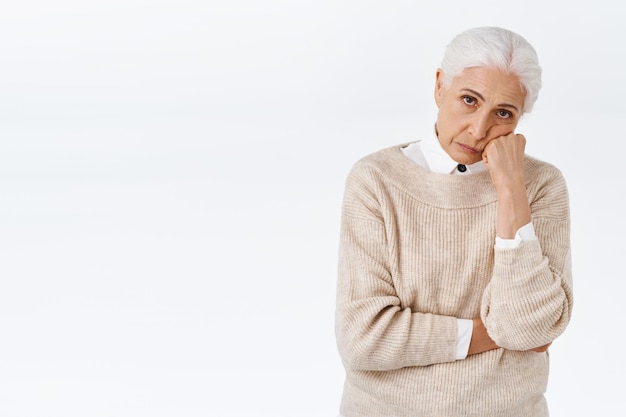 Bored or annoyed senior lady with grey combed hair, lean face on fist, look from under forehead distressed with frustration and bad mood