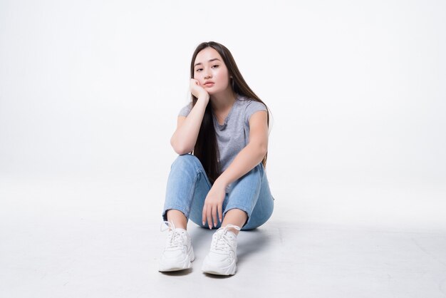 Bored asian woman sitting on floor isolated on white wall.