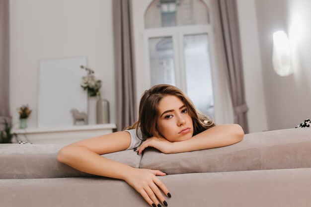 Bored brunette woman with black nails lying on sofa