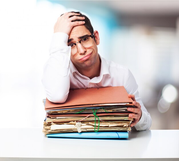 Bored man looking at a pile of papers with one hand on his forehead