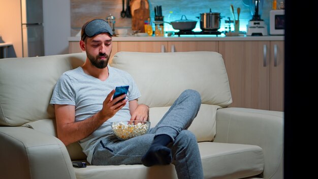 Bored man sitting on couch holding popcorn bowl