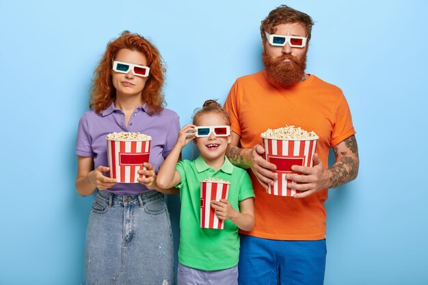 Bored mum and dad being indifferent while their daughter watches interesting cartoon in cinema, wear three dimension glasses, bright casual summer clothes, spend spare time for entertainment