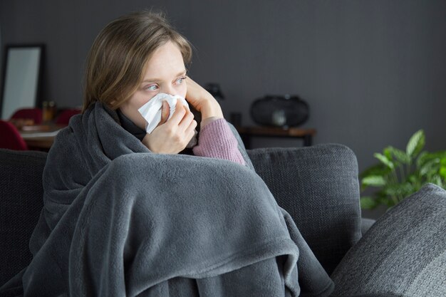 Bored sick woman holding hand at head, blowing nose with napkin