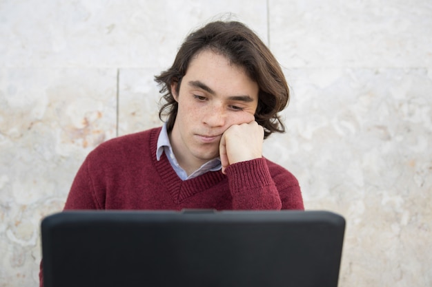 Tipo adolescente annoiato che per mezzo del computer portatile all'aperto