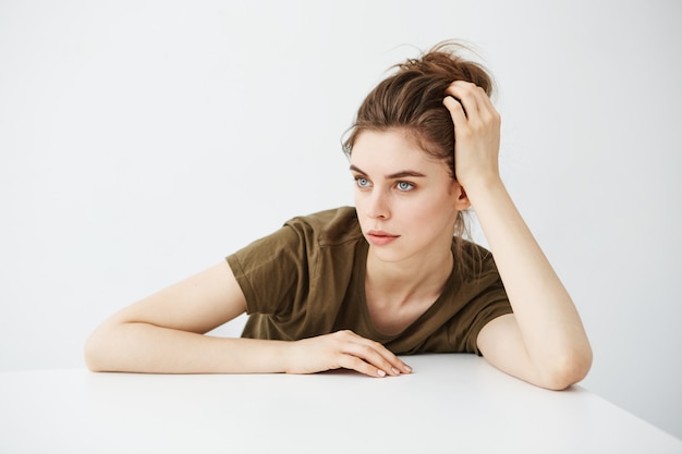 Free photo bored tired dull young woman student with bun sitting at table over white background.