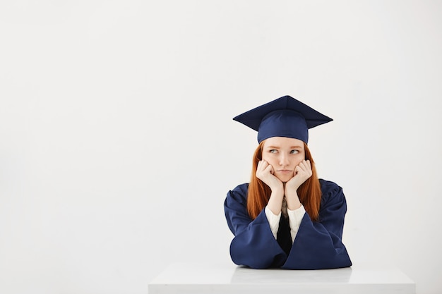 Bored tired female graduate thinking sitting over white backround Copy space.