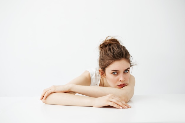 Bored tired young pretty woman with bun thinking dreaming lying on table over white background.