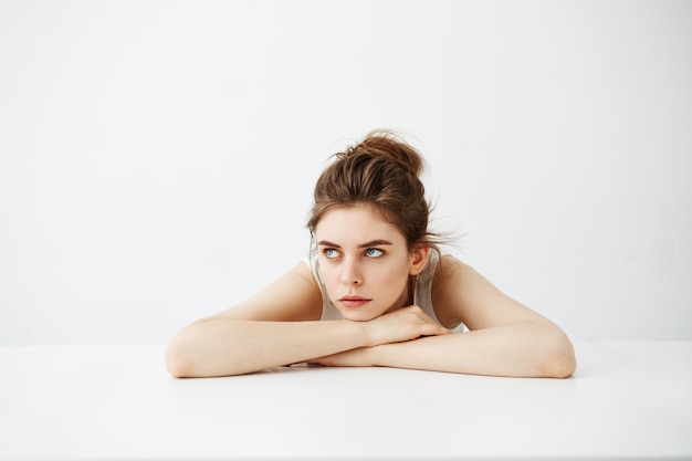 Bored tired young pretty woman with bun thinking dreaming lying on table over white background.