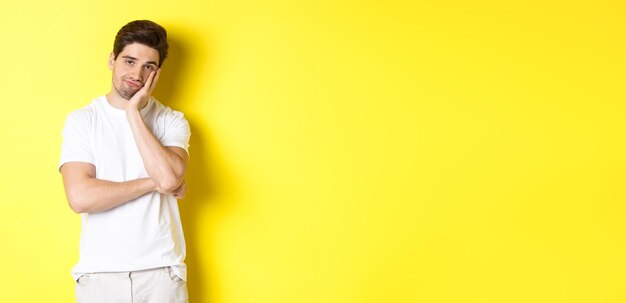 Free photo bored and unamused man looking with indifference standing in white clothes over yellow background