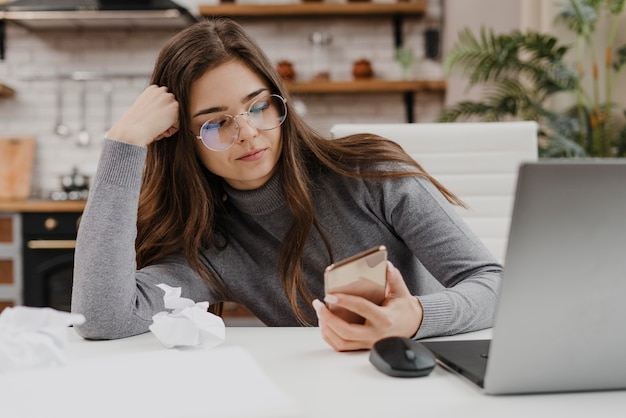 Donna annoiata che controlla il suo telefono mentre lavora da casa