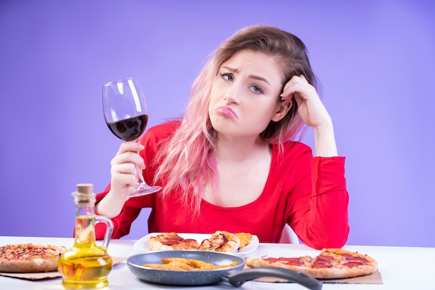 La donna annoiata in camicetta rossa si siede al tavolo con un bicchiere di vino rosso