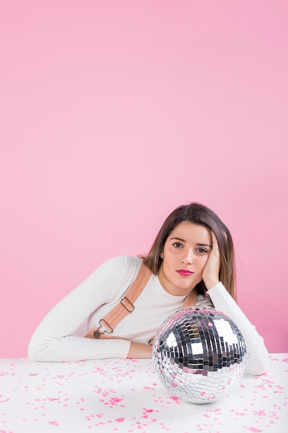 Free photo bored woman sitting at table with shiny disco ball