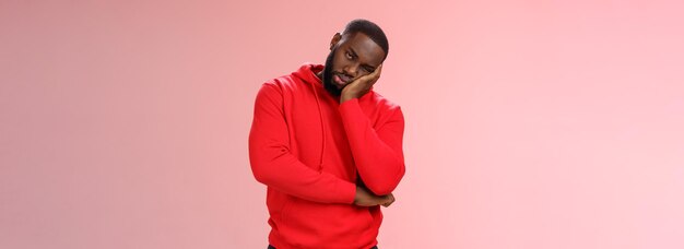 Bored young s black guy in red hoodie facepalm lean head hand look indifferent sleepy attend boring 